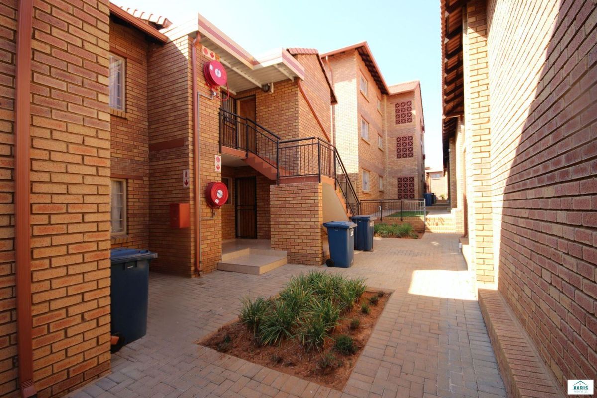 Exterior view of a brick apartment complex featuring a paved courtyard, external staircases, and communal access areas.