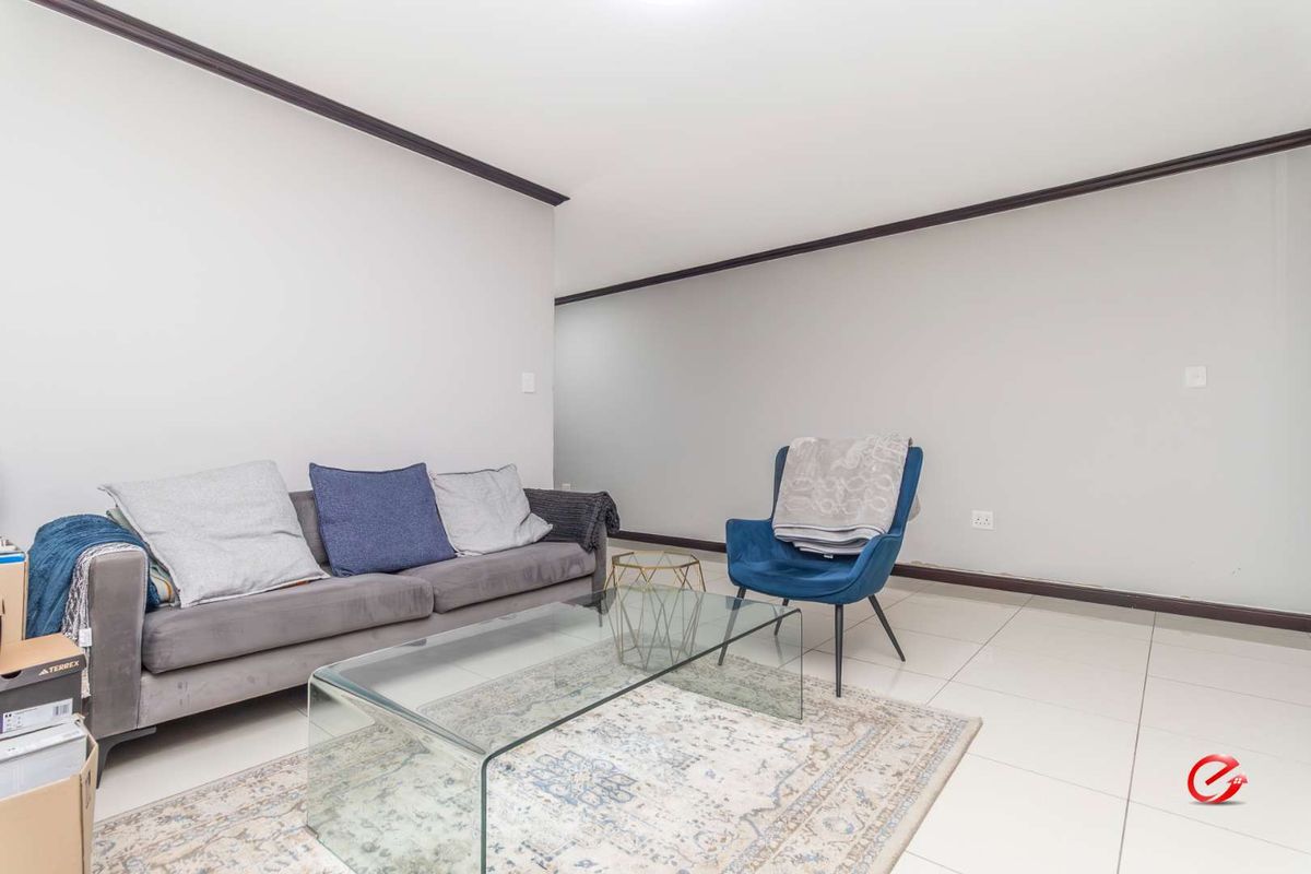A bright living room featuring neutral tiled flooring and dark contrasting crown molding, providing a clean and versatile space for relaxation.