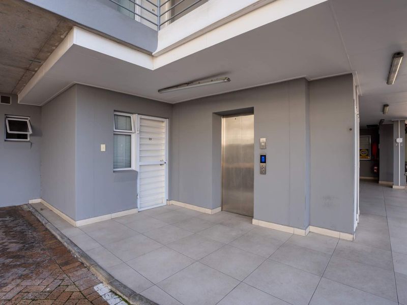 Modern apartment building entrance featuring a secure access door, stainless steel elevator, and clean tiled flooring in a well-maintained common area.