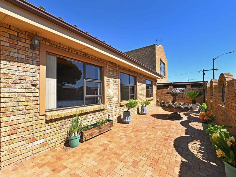A well-maintained paved patio area featuring face brick walls, aluminium window frames, and a decorative stone fountain.