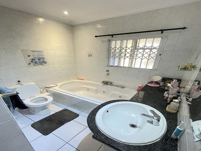 A functional bathroom featuring a built-in bathtub, vanity sink with granite countertop, and tiled finishes throughout.