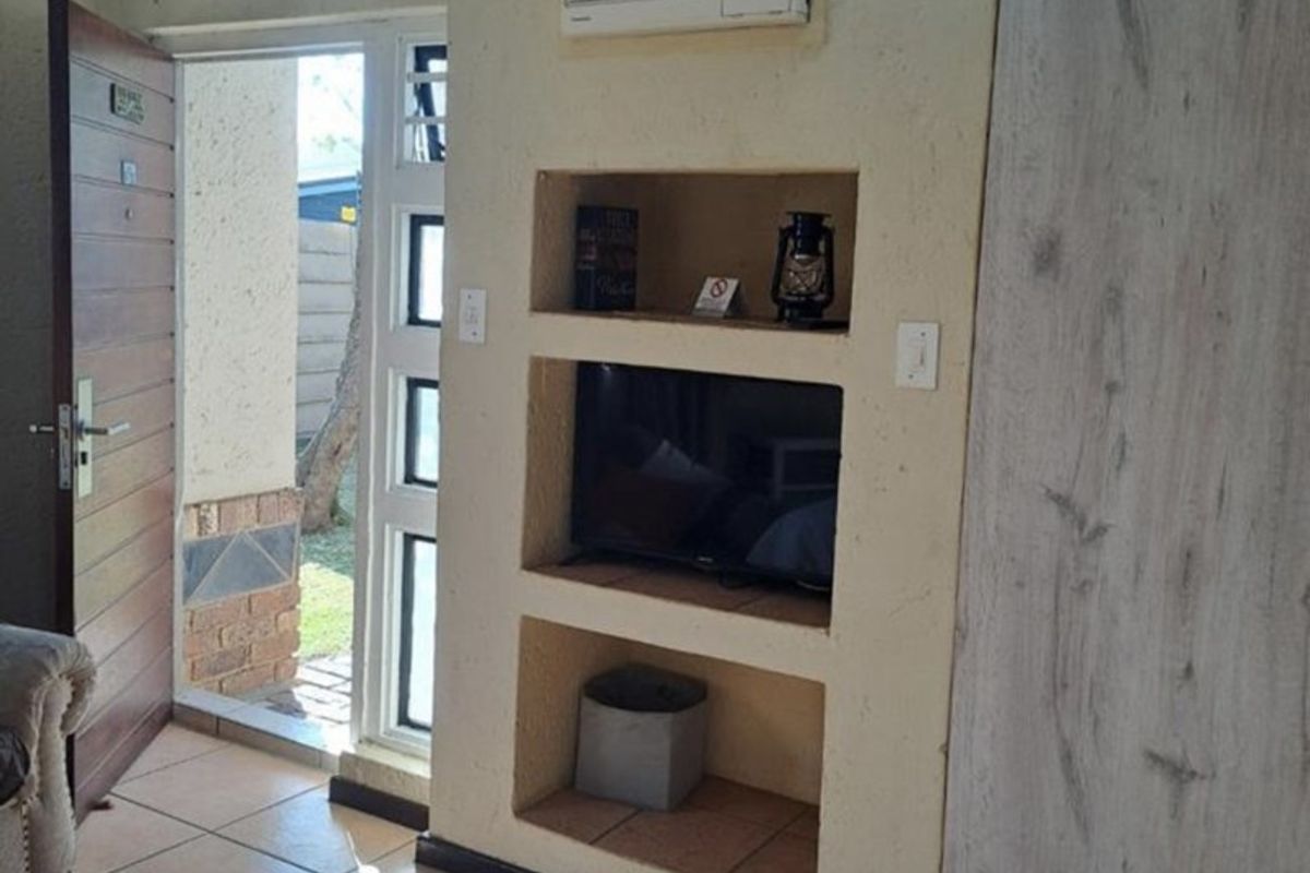 Living area featuring built-in wall shelving, an integrated air conditioning unit, tiled flooring, and direct access to the exterior through a wooden door.