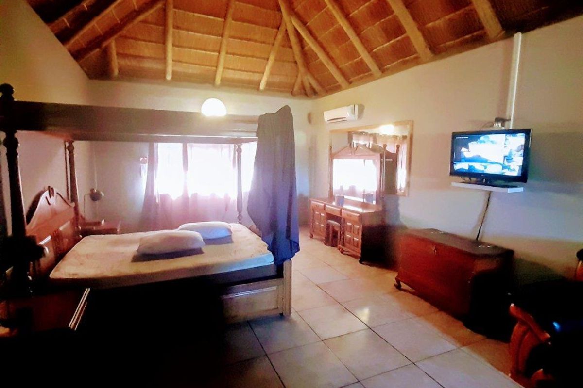 Spacious bedroom featuring a high vaulted thatched ceiling, tiled flooring, and a wall-mounted air conditioning unit.