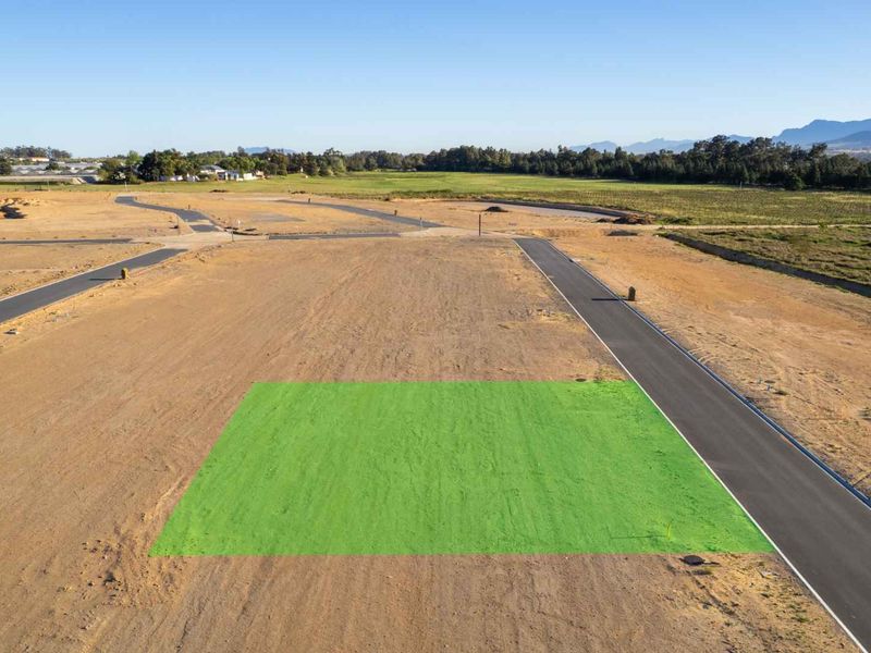 Aerial view of a vacant residential plot in a new development, featuring paved road access and clear boundaries.