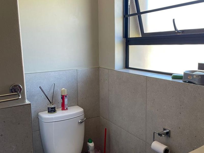 A compact bathroom featuring modern grey wall tiles, a white toilet, and a vanity unit with a top-hung window for natural light.