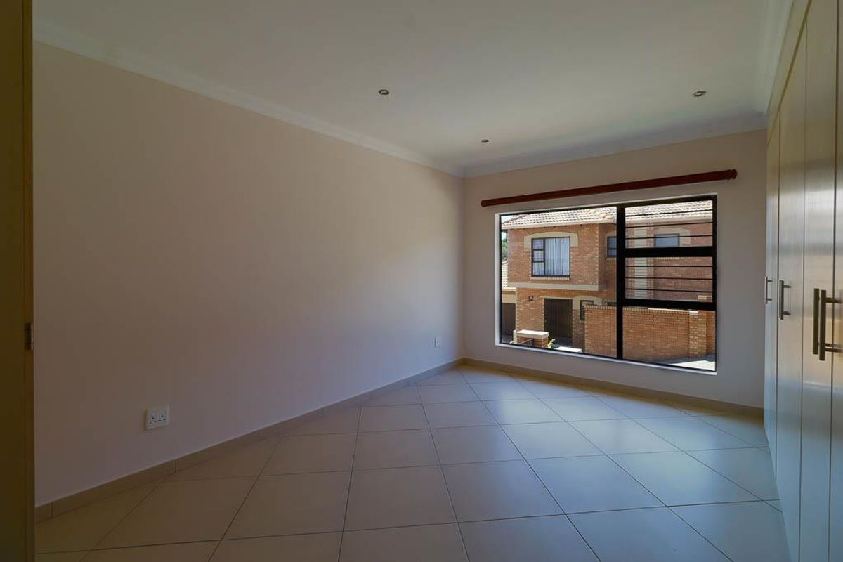 A bright, empty bedroom featuring neutral tiled flooring, built-in cupboards, and recessed downlights, offering a clean and versatile space.