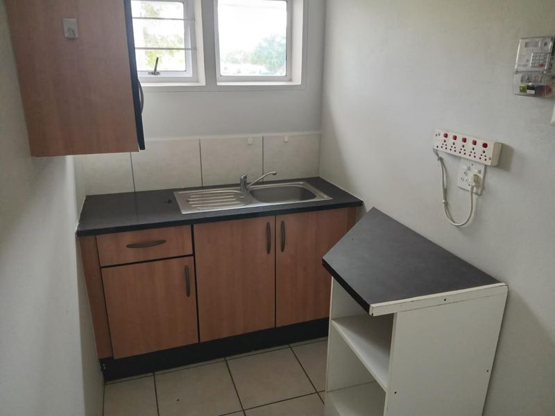 A functional scullery area featuring laminate cabinetry, a stainless steel sink, tiled splashback, and tiled flooring, suitable for utility or prep work.