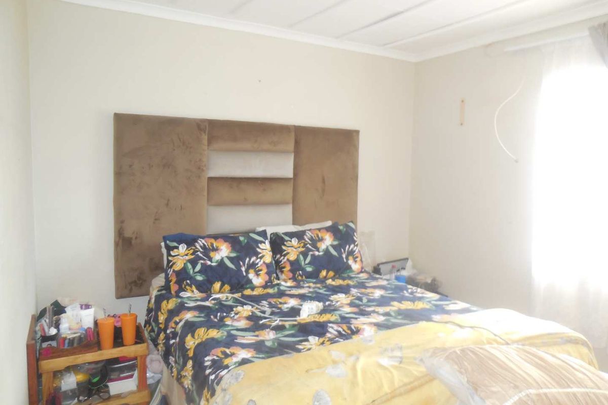 A bedroom featuring a wall-mounted headboard and natural light from the window, requiring minor cosmetic updates and electrical finishing.
