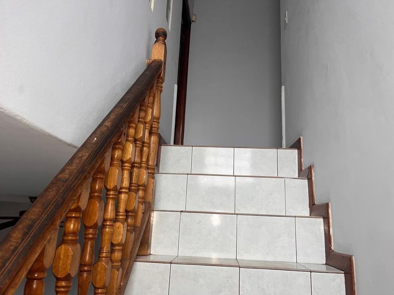 A staircase featuring tiled steps and a traditional wooden balustrade, showing signs of wear on the handrail and trim.