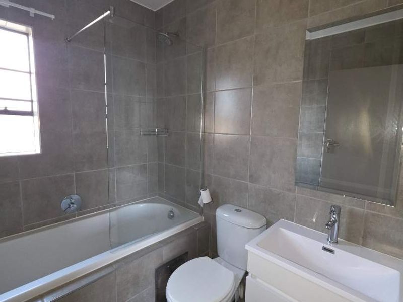 Modern bathroom featuring a bathtub with a glass shower screen, a wall-mounted vanity with a basin, and neutral floor-to-ceiling wall tiles.
