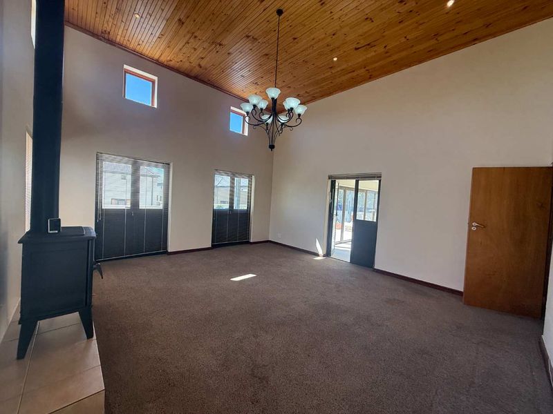 Spacious living room featuring a high timber-clad vaulted ceiling, a wood-burning fireplace, and neutral walls, offering a bright and open atmosphere.