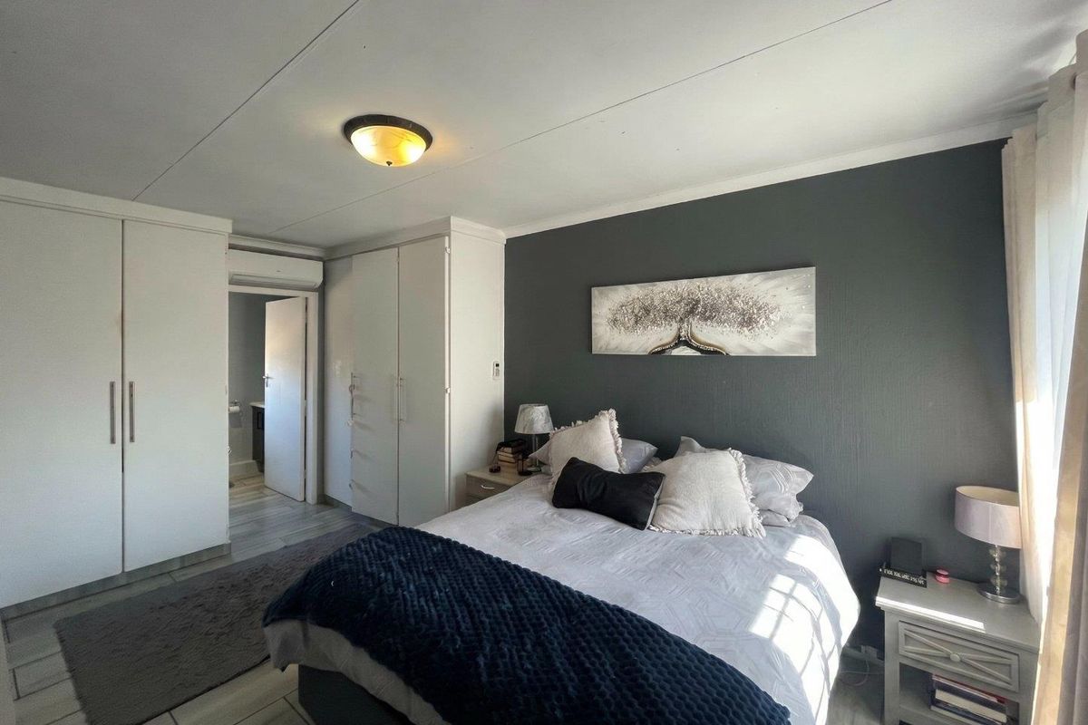 A well-maintained bedroom featuring built-in cupboards, tiled flooring, and an air conditioning unit, with direct access to an en-suite bathroom.