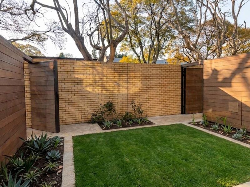 A well-maintained private garden featuring a manicured lawn, landscaped garden beds, and a combination of brick and timber-clad boundary walls.