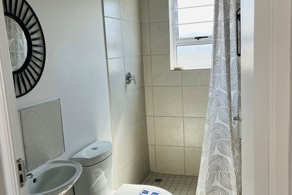 A compact bathroom featuring a tiled shower enclosure, wall-mounted basin, and toilet. The space requires maintenance and cosmetic updates.