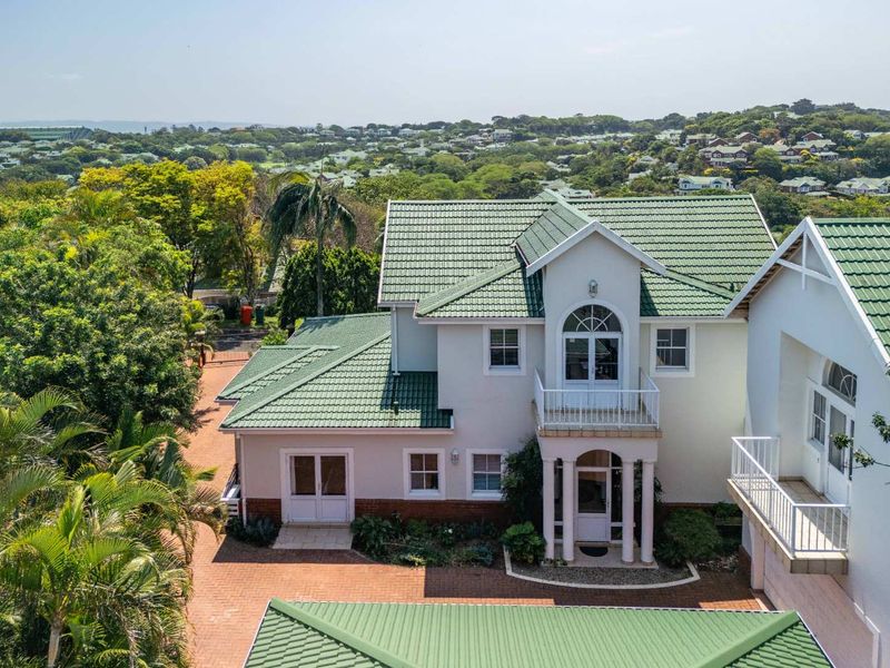 Aerial view of a two-story residential property featuring a green tiled roof, brick paved driveway, and a balcony with architectural detailing.