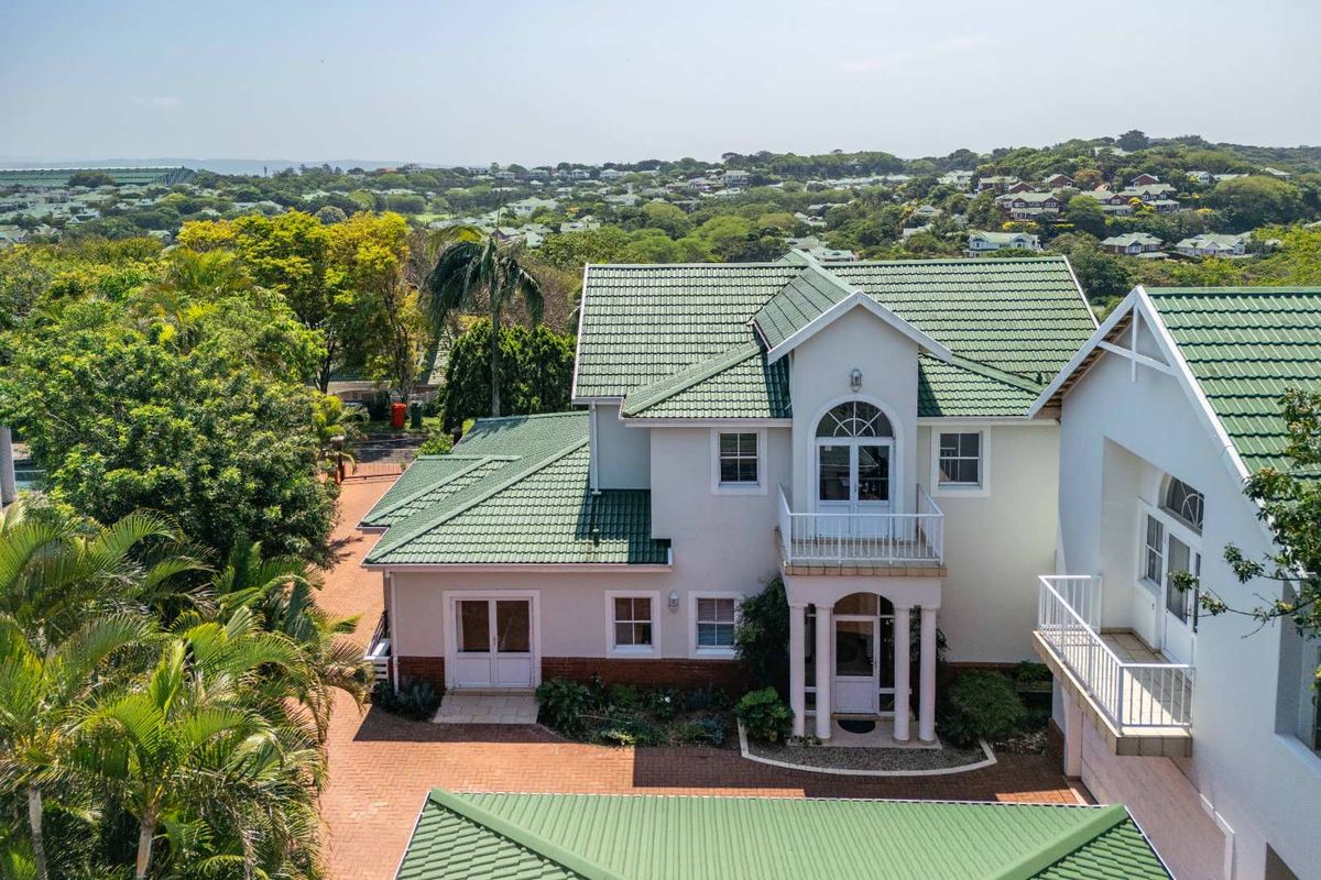 Aerial view of a two-story residential property featuring a green tiled roof, brick paved driveway, and a balcony with architectural detailing.