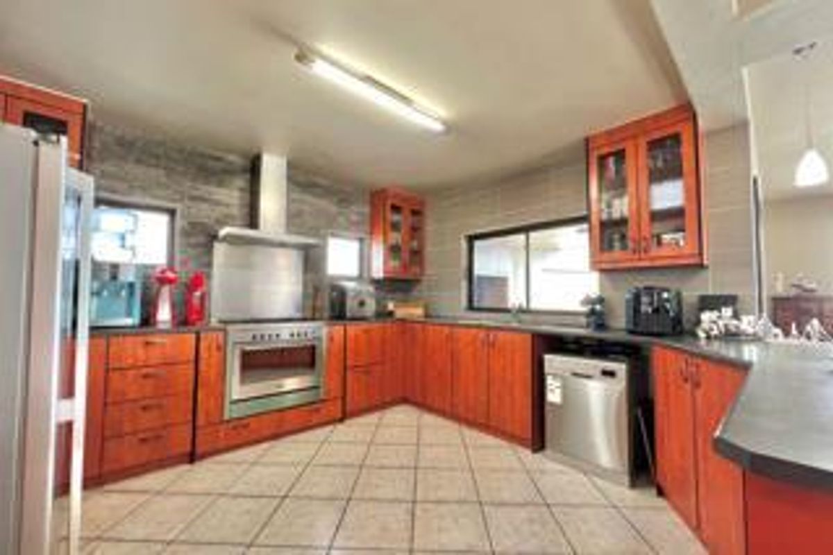 Spacious kitchen featuring wood-toned cabinetry, stainless steel oven with extractor fan, tiled flooring, and ample countertop workspace.