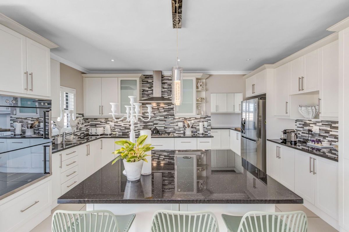 Modern kitchen featuring a large central island with a dark stone countertop, white cabinetry, stainless steel appliances, and a decorative mosaic tile backsplash.