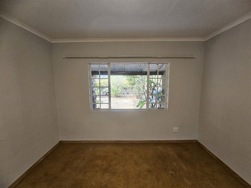 A clean, empty bedroom featuring neutral walls, a large window with a curtain rail, and simple flooring, offering a blank canvas for personalization.