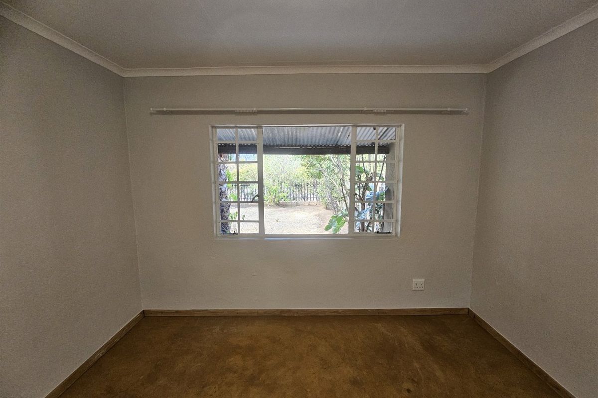 A clean, empty bedroom featuring neutral walls, a large window with a curtain rail, and simple flooring, offering a blank canvas for personalization.
