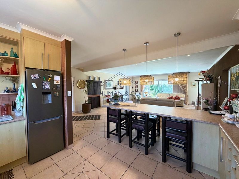 Spacious open-plan living area featuring a functional kitchen with breakfast bar, tiled flooring, and integrated lighting, flowing seamlessly into the adjacent lounge space.