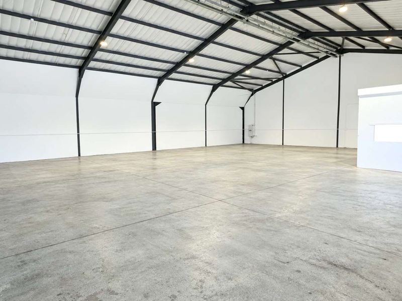 Spacious industrial warehouse unit featuring high ceilings with exposed steel portal framing, polished concrete flooring, and a dedicated internal office enclosure.