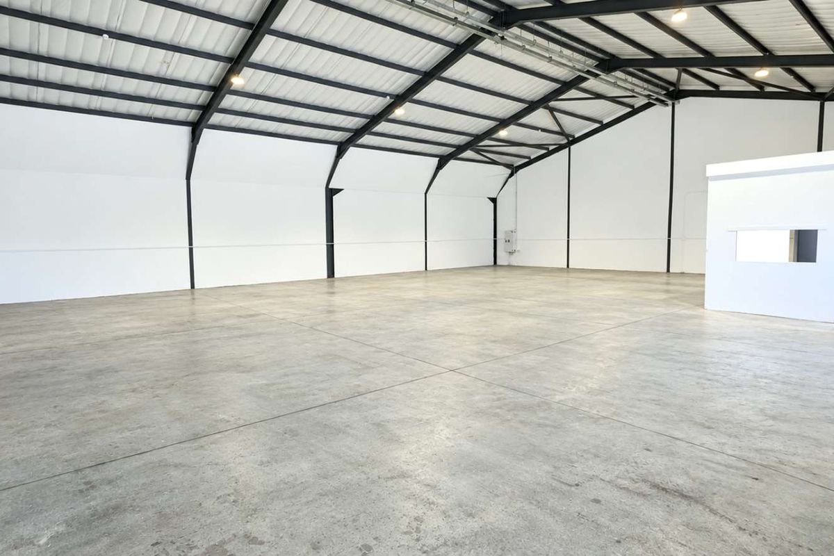 Spacious industrial warehouse unit featuring high ceilings with exposed steel portal framing, polished concrete flooring, and a dedicated internal office enclosure.