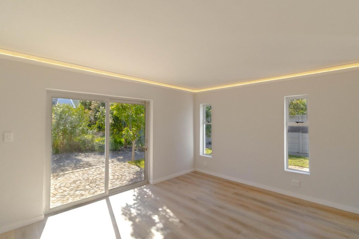 Bright and modern living area featuring light laminate flooring, recessed cove lighting, and sliding glass doors providing direct access to the garden.