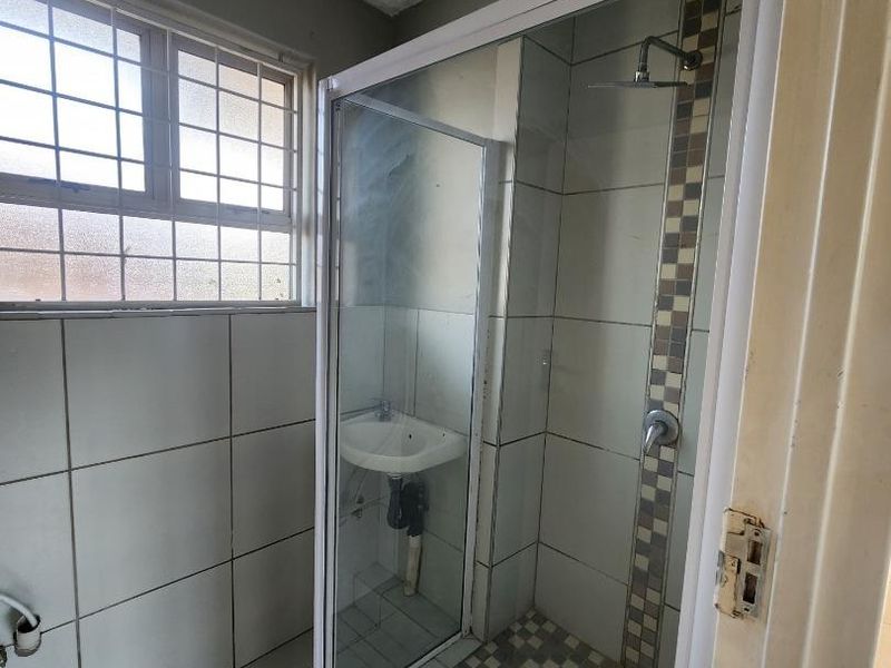 A functional bathroom featuring a shower enclosure and wall-mounted basin, requiring cosmetic updates to modernize the finishes and fixtures.