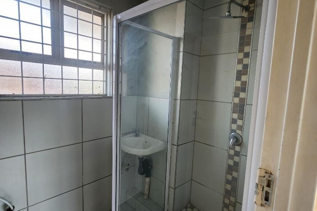 A functional bathroom featuring a shower enclosure and wall-mounted basin, requiring cosmetic updates to modernize the finishes and fixtures.