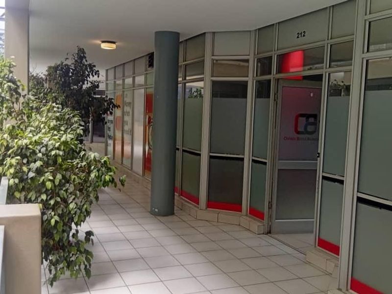 Exterior office corridor featuring tiled flooring, glass partition walls, and access to an escalator in a commercial building setting.