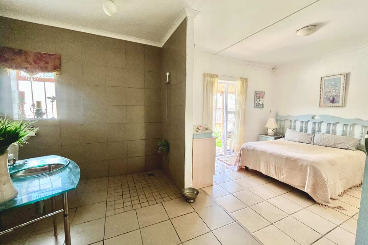 A bedroom featuring an open-plan layout with an integrated walk-in shower, tiled flooring, and direct access to an outdoor area via a sliding glass door.