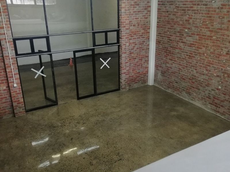 Modern industrial-style office space featuring exposed brick walls, polished concrete floors, and a sleek black-framed glass partition.