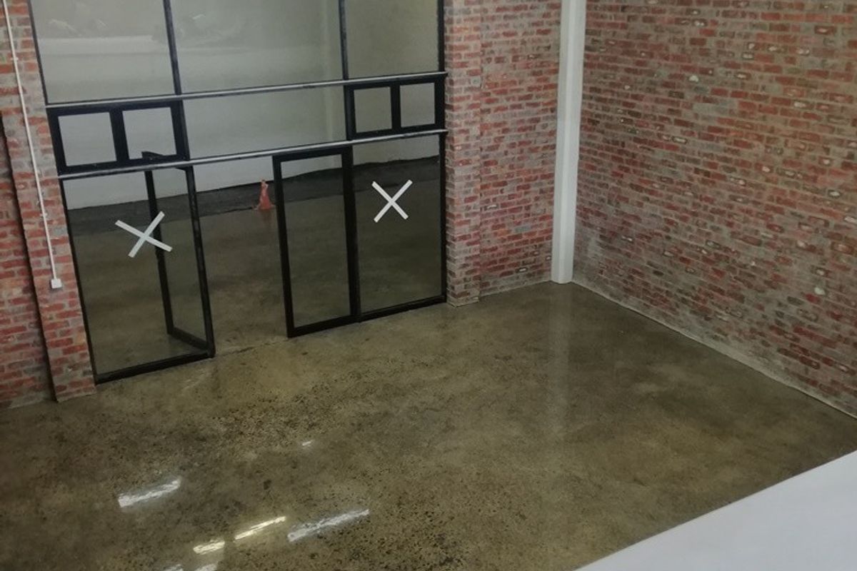 Modern industrial-style office space featuring exposed brick walls, polished concrete floors, and a sleek black-framed glass partition.