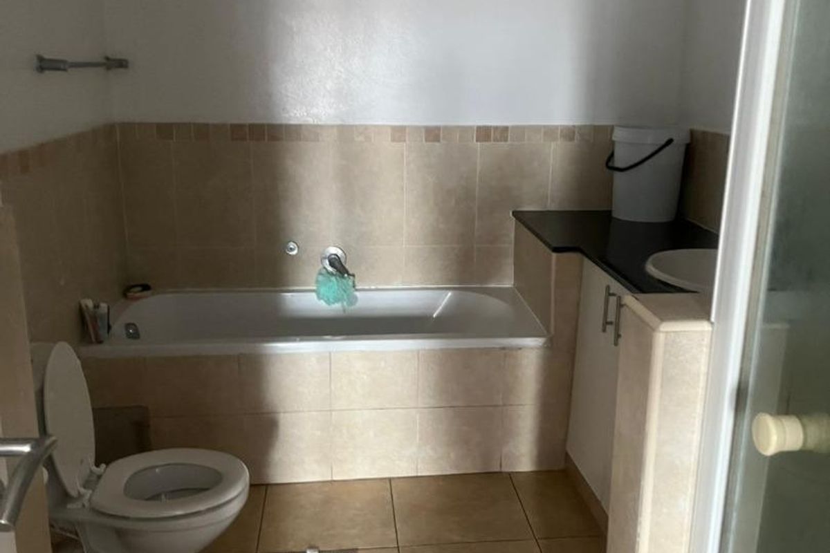 A functional bathroom featuring a built-in bathtub, vanity cabinet, and toilet, with visible signs of ceiling wear requiring maintenance.