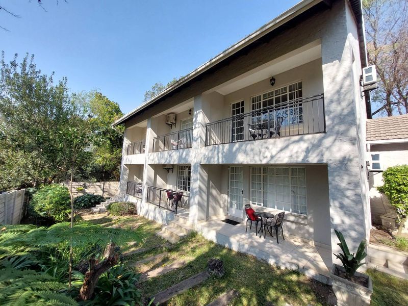 Rear view of a two-story apartment building featuring ground floor patios and upper-level balconies with metal railings, set against a landscaped garden area.