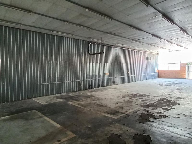 Spacious industrial utility area featuring corrugated metal walls, concrete flooring, and overhead fluorescent lighting, suitable for warehouse or workshop use.