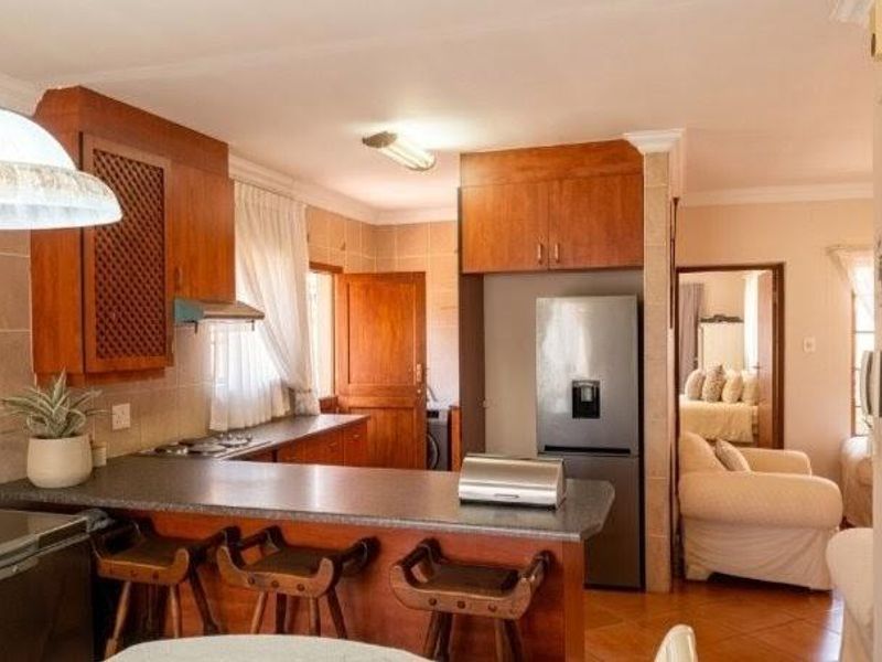 Open plan kitchen featuring wooden cabinetry, a breakfast bar, and tiled flooring, seamlessly connecting to the adjacent living area.