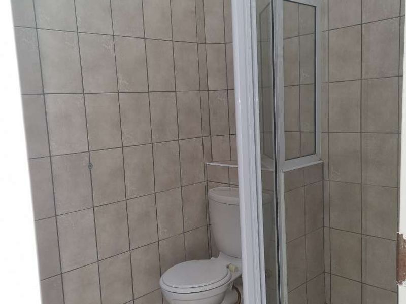 A functional bathroom featuring a shower enclosure and toilet with neutral wall and floor tiling.