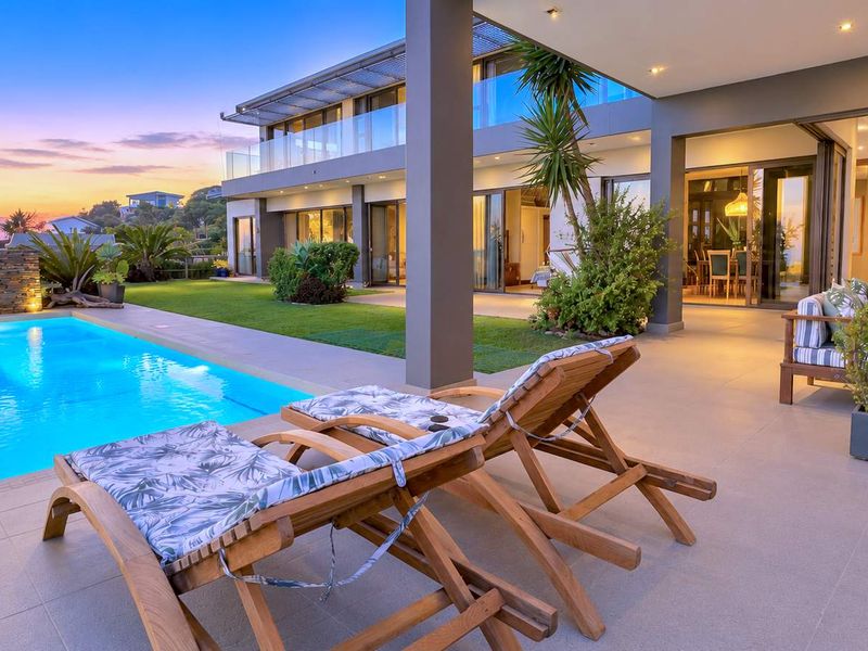 A luxurious outdoor pool area featuring a modern swimming pool, stone accent wall, and a spacious tiled patio overlooking the multi-level residence.
