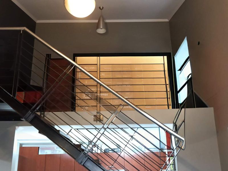A modern open-plan living area featuring a prominent staircase with a stainless steel balustrade leading to a mezzanine level.
