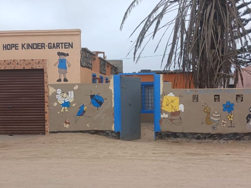 Front facade of a commercial kindergarten property featuring a roller shutter garage door, boundary wall with decorative murals, and a pedestrian entrance gate.