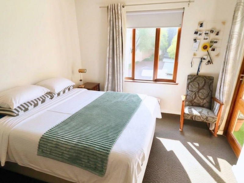 A well-lit bedroom featuring carpet flooring, timber window and door frames, and direct access to an outdoor area.