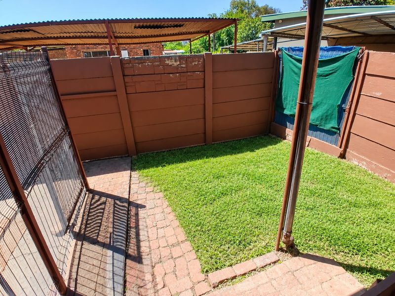 A small private garden area featuring brick paving, a lawn, and precast concrete boundary walls.