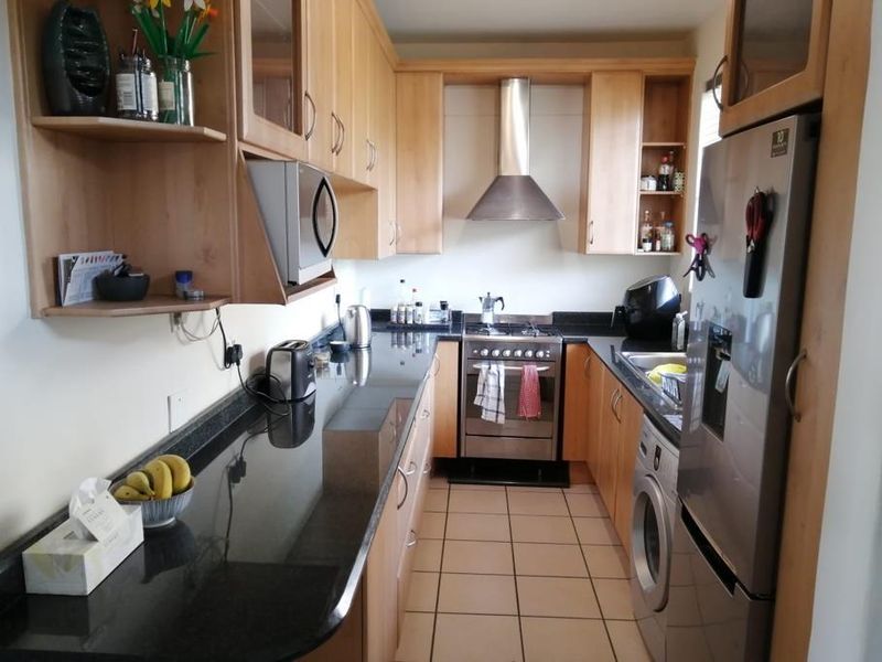A functional galley-style kitchen featuring light wood cabinetry, dark granite countertops, stainless steel appliances, and tiled flooring.