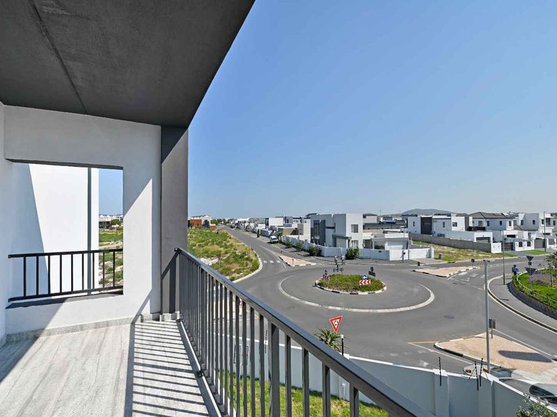 A modern, clean balcony with tiled flooring and a metal balustrade, offering an elevated view of the surrounding residential neighbourhood and street infrastructure.