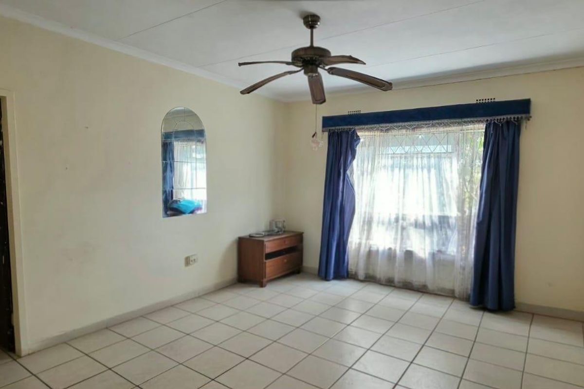 A spacious living room featuring tiled flooring, a ceiling fan, and a recessed wall mirror, offering a blank canvas for potential interior updates.