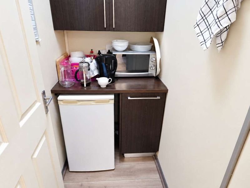 A compact kitchenette or scullery area featuring dark wood-finish cabinetry and a laminate countertop, providing functional storage and preparation space.