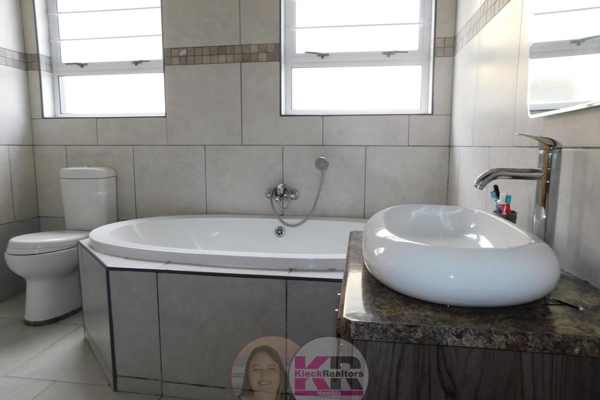 A well-maintained bathroom featuring a built-in bathtub, a modern vessel sink on a vanity, and tiled walls with large windows for natural light.