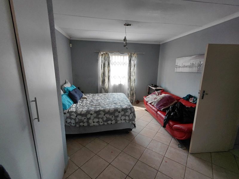 A bedroom featuring tiled flooring, a built-in wardrobe, and a window with curtains. The room requires a new light fixture.